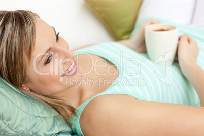 Smiling woman drinking a coffee lying on a sofa