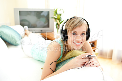 Cheerful blond woman listening music lying on a sofa