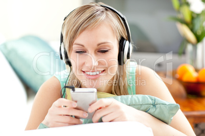 Smiling blond woman listening music lying on a sofa