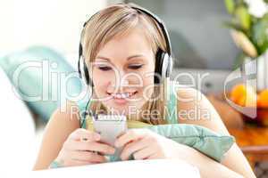 Smiling blond woman listening music lying on a sofa