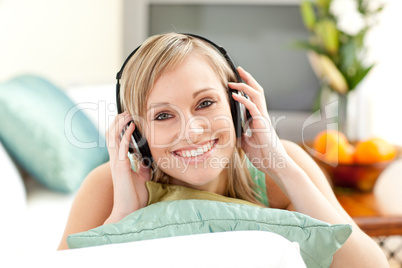 Happy blond woman listening music lying on a sofa