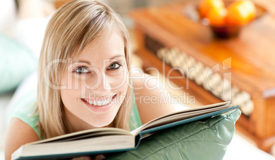 Happy woman lying on a sofa reading a book