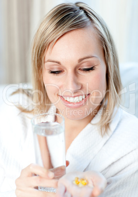 Sick blond woman holding a glass of water and pills