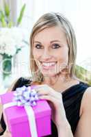 Glowing woman opening a gift sitting on a sofa