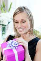 Happy woman opening a gift sitting on a sofa