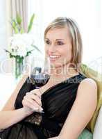 Happy woman drining red wine sitting on a sofa