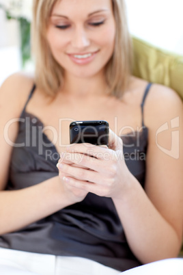 Blond woman sending a text sitting on a sofa