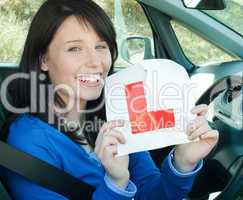 Happy teen girl sitting in her car tearing a L-sign