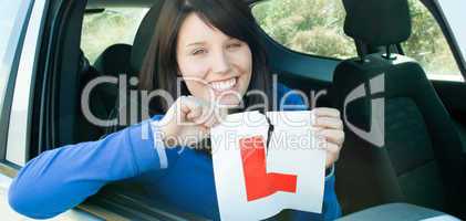 Smiling teen girl sitting in her car tearing a L-sign