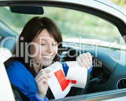 Brunette teen girl sitting in her car tearing a L-sign