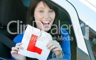 Happy brunette teen girl sitting in her car tearing a L-sign