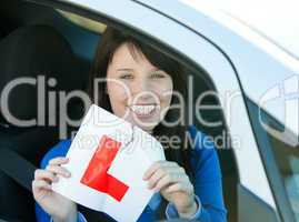 Smiling brunette teen girl sitting in her car tearing a L-sign