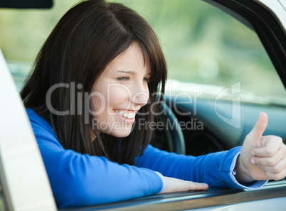 Smiling teen girl with a thumb up sitting in her car