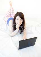 Pensive woman surfing the internet lying on a bed