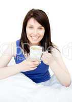 Happy woman drinking a coffee sitting on her bed