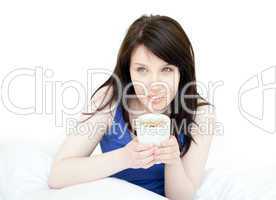 Charming woman drinking a coffee sitting on her bed