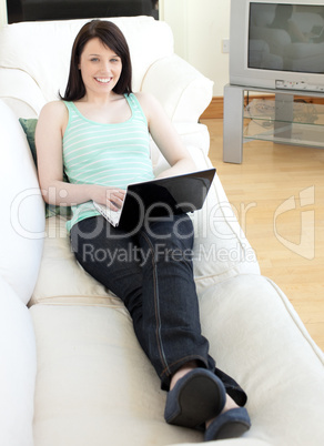 Smiling woman surfing the internet lying on a sofa