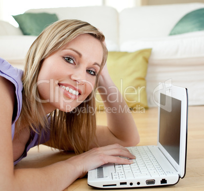 Cheerful blond woman using a laptp lying on the floor