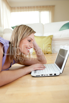 Happy blond woman using a laptp lying on the floor