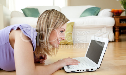 Smiling blond woman using a laptp lying on the floor