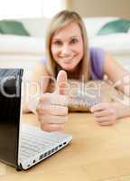 Cheerful blond woman shopping on-line lying on the floor
