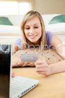 Smiling woman shopping on-line lying on the floor