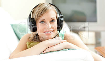 Happy young woman listening music lying on a sofa