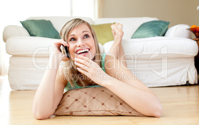 Laughing young woman talking on phone lying on the floor