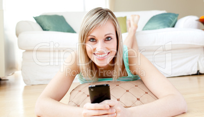 Joyful woman sending a text lying on the floor