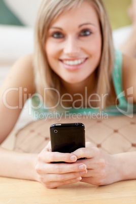 Attractive blond woman sending a text lying on the floor