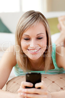 Cheerful woman sending a text lying on the floor