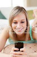 Cheerful woman sending a text lying on the floor