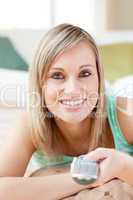 Charming blond woman watching TV lying on the floor