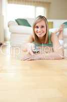 Pretty young woman watching TV lying on the floor