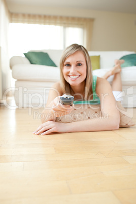 Jolly young woman watching TV lying on the floor