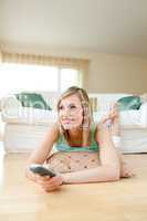 Attractive young woman watching TV lying on the floor