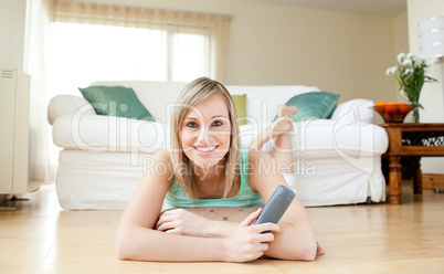 Happy young woman watching TV lying on the floor