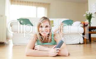 Happy young woman watching TV lying on the floor