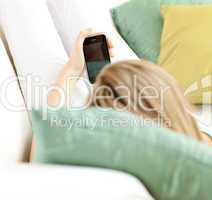 Blond woman sending a text lying on a sofa