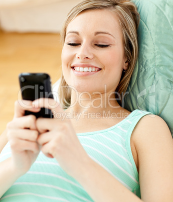 Smiling young woman sending a text lying on a sofa