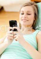 Bright young woman sending a text lying on a sofa