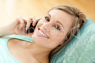 Happy young woman talking on phone lying on a sofa