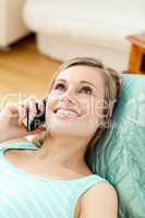 Smiling young woman talking on phone lying on a sofa