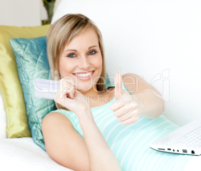 Cheerful woman shopping on-line lying on a sofa