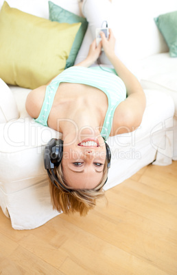 Laughing young woman listening music lying on a sofa