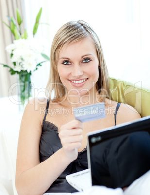Joyful blond woman shopping on-line sitting on a sofa