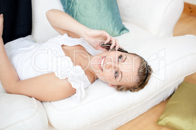 Radiant young woman talking on phone lying on a sofa