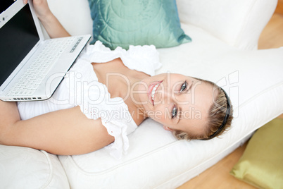 Cute blond woman surfing the internet lying on a sofa