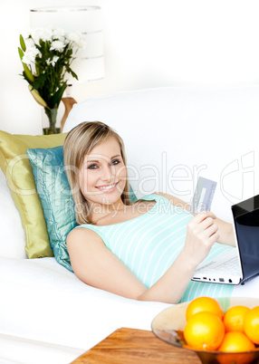 Happy woman shopping on-line lying on a sofa