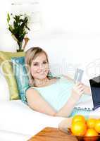 Happy woman shopping on-line lying on a sofa